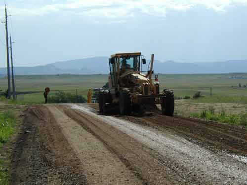 A tractor pushes dirt to level out a country road